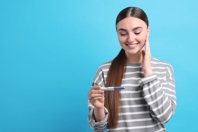 Photo of Happy woman holding pregnancy test on light blue background, space for text