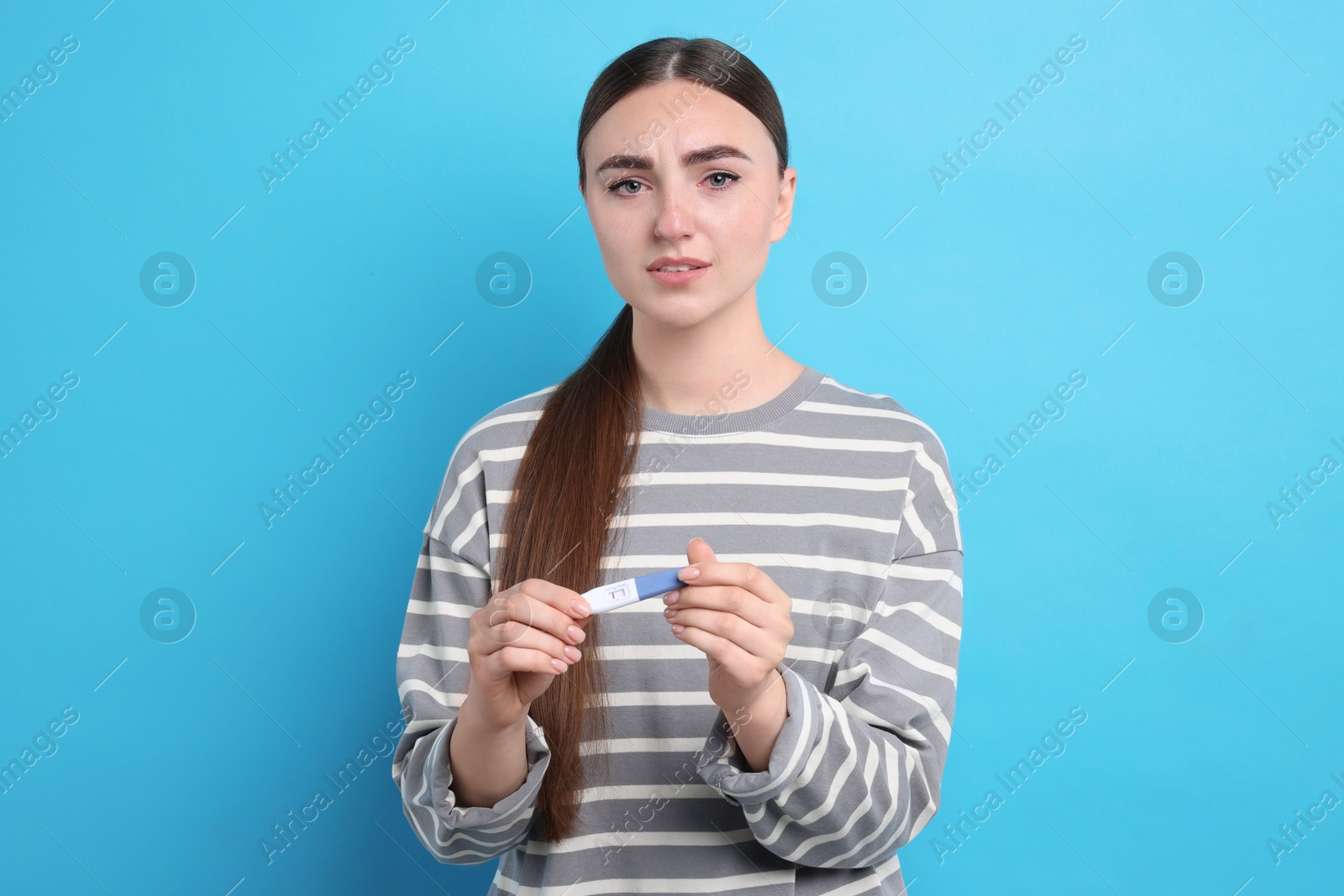 Photo of Sad woman holding pregnancy test on light blue background