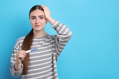 Photo of Sad woman holding pregnancy test on light blue background, space for text