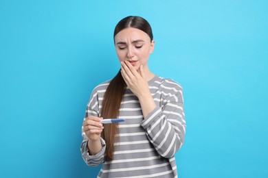 Sad woman holding pregnancy test on light blue background