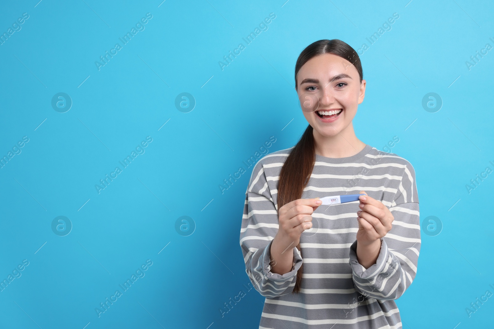 Photo of Happy woman holding pregnancy test on light blue background, space for text