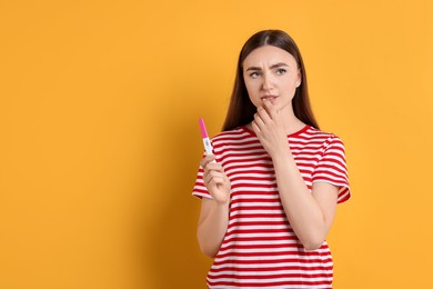 Photo of Sad woman holding pregnancy test on orange background, space for text