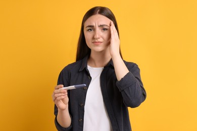 Photo of Sad woman holding pregnancy test on orange background