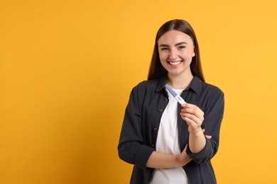 Happy woman holding pregnancy test on orange background, space for text