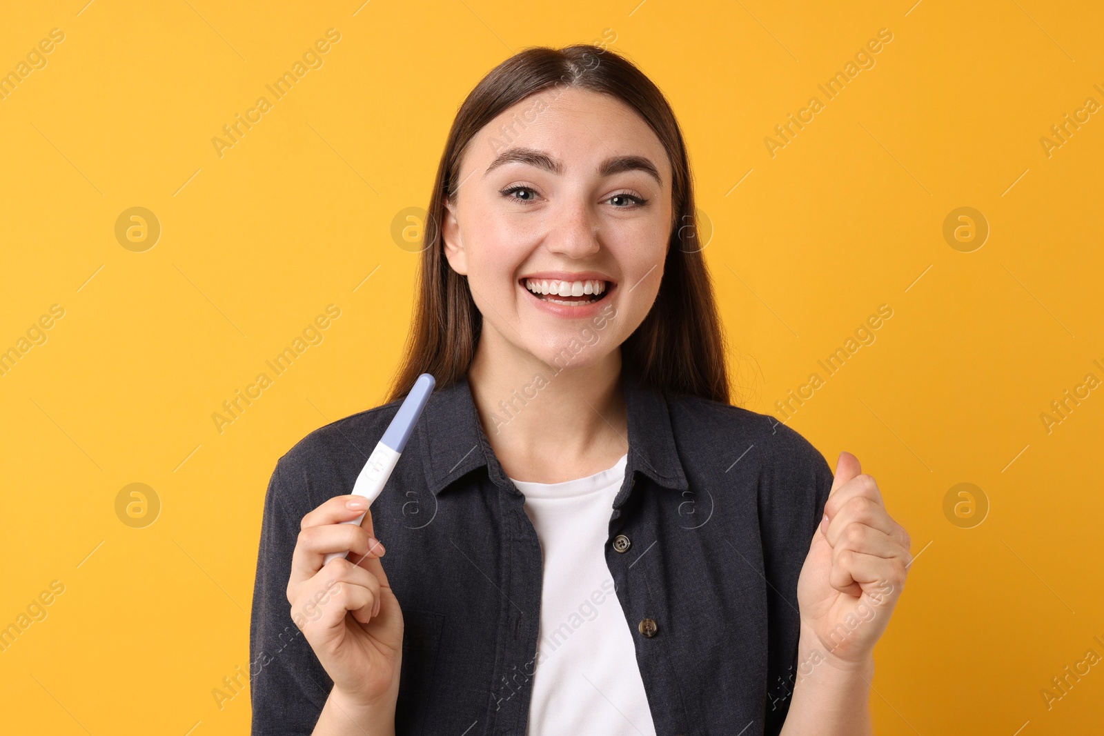 Photo of Happy woman holding pregnancy test on orange background