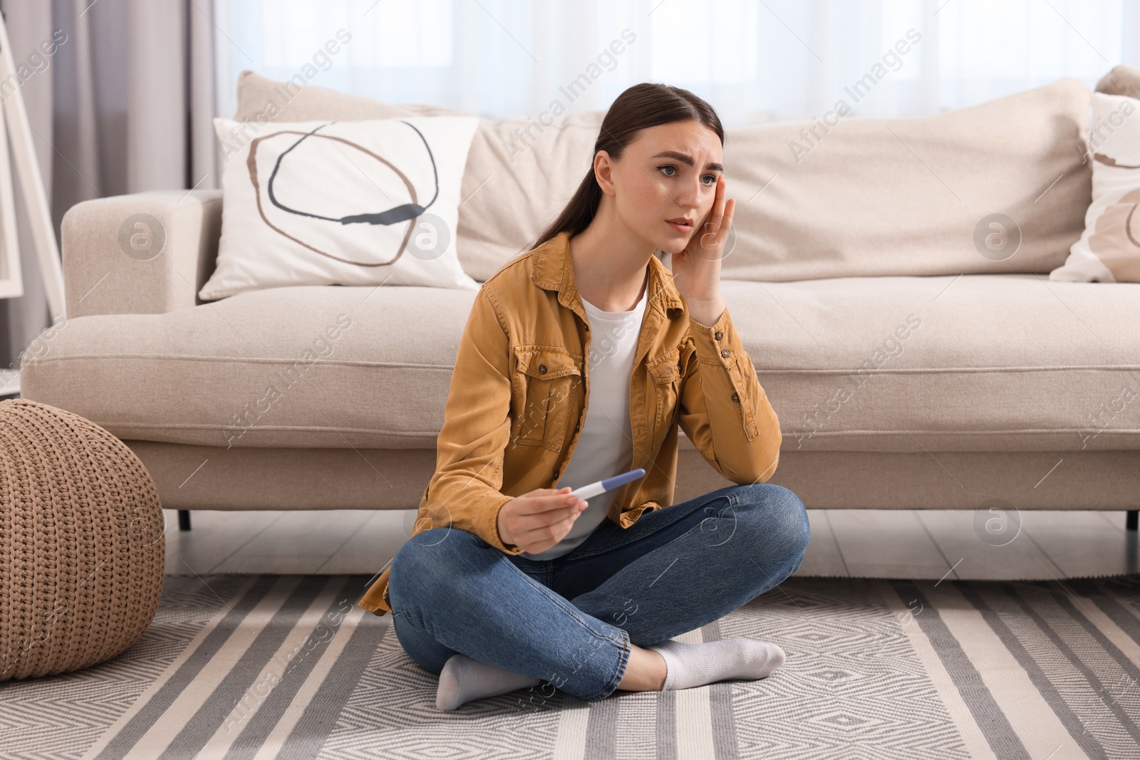 Photo of Sad woman holding pregnancy test on floor indoors