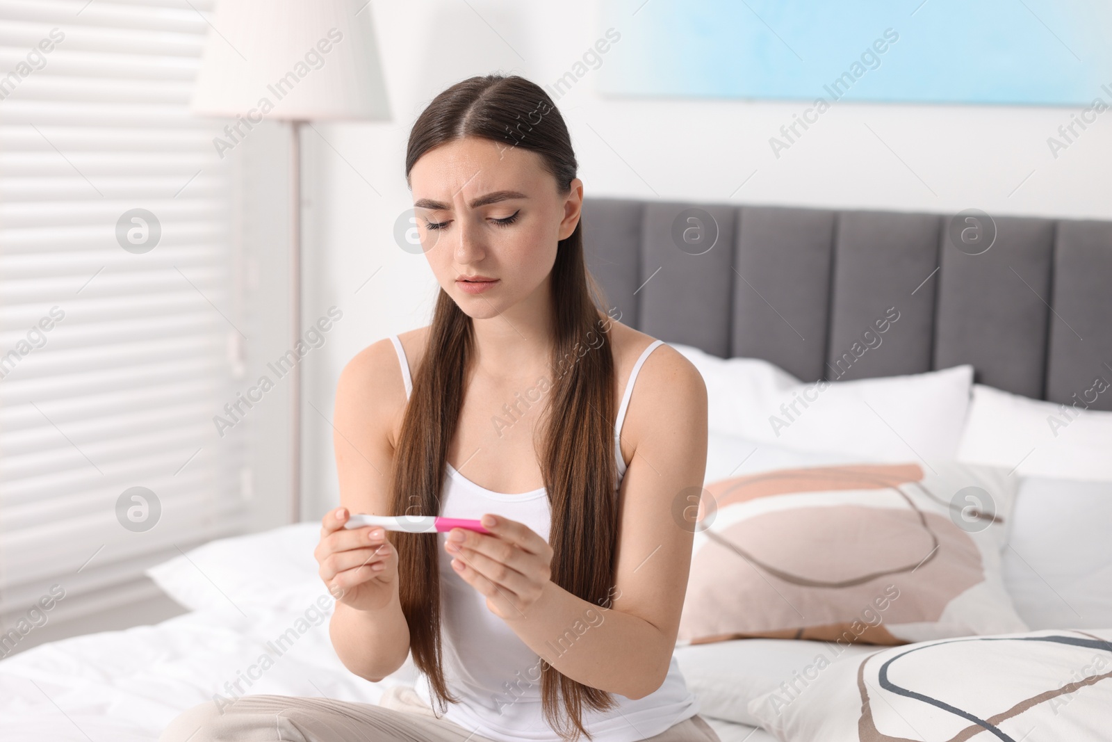 Photo of Sad woman holding pregnancy test on bed in room