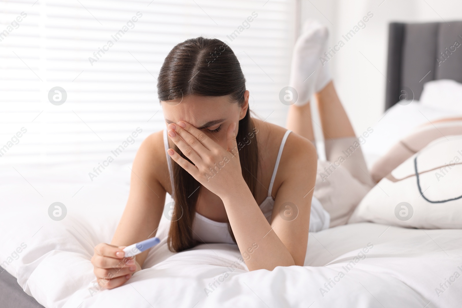 Photo of Sad woman holding pregnancy test on bed in room