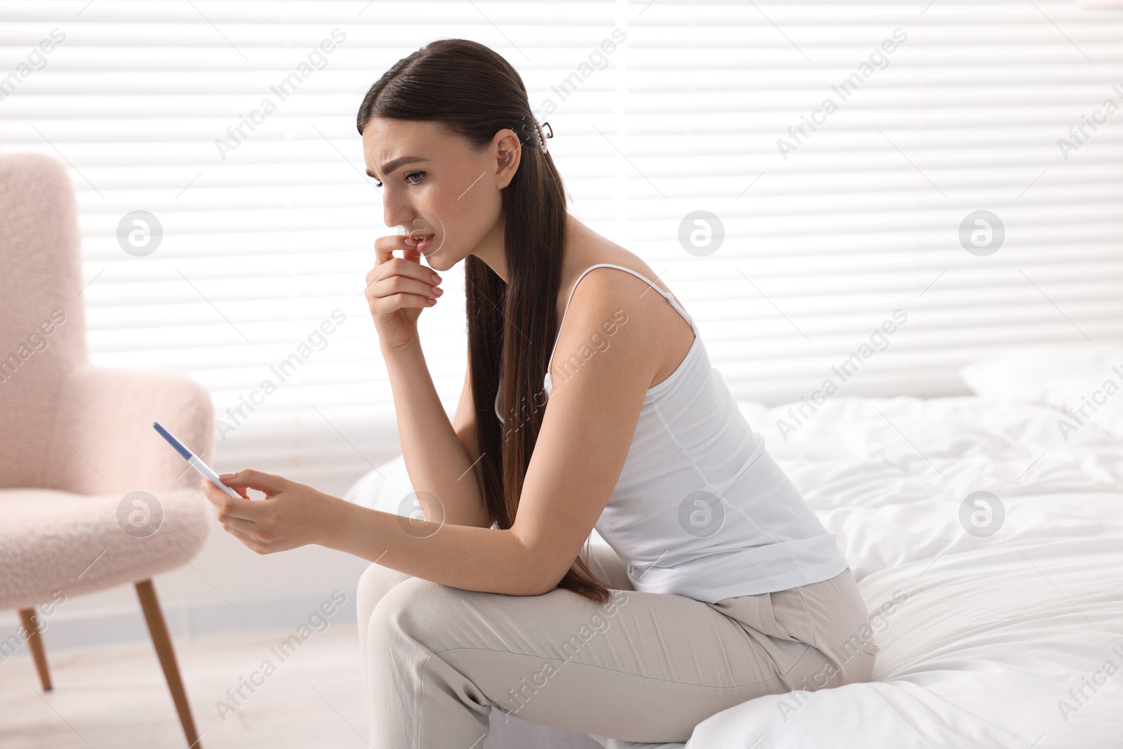 Photo of Sad woman holding pregnancy test on bed in room