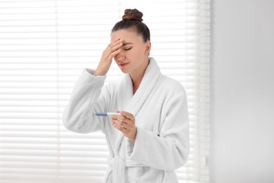 Sad woman holding pregnancy test in bathroom