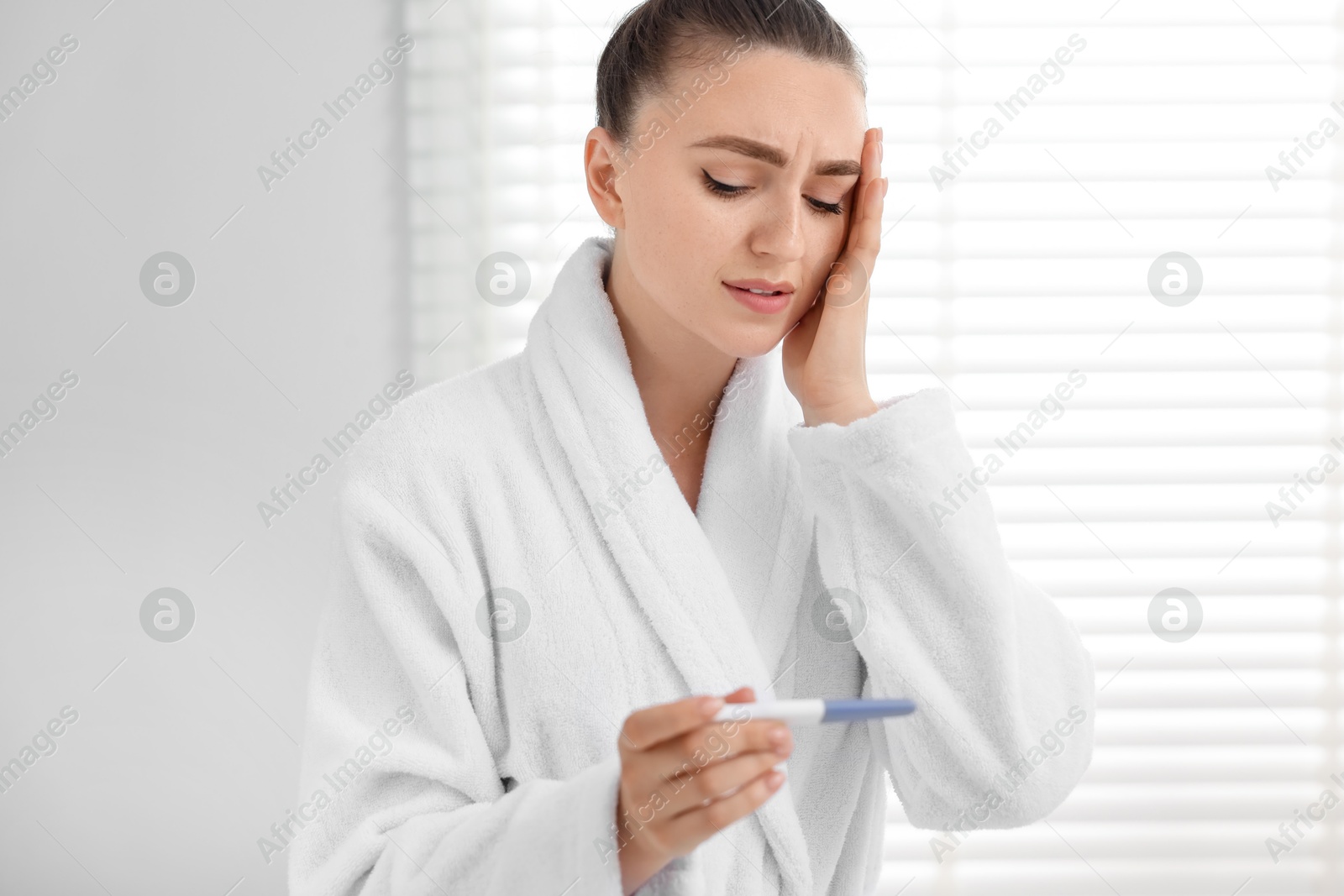 Photo of Sad woman holding pregnancy test in bathroom