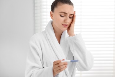 Sad woman holding pregnancy test in bathroom