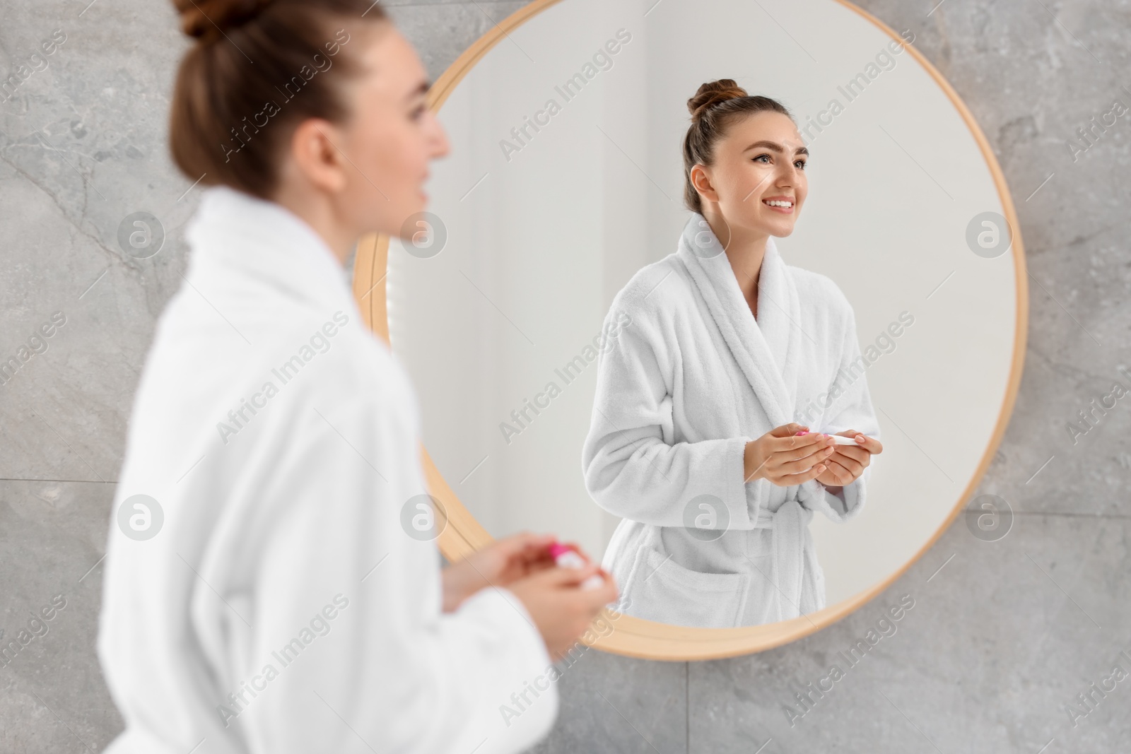 Photo of Happy woman holding pregnancy test near mirror in bathroom