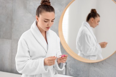 Photo of Sad woman holding pregnancy test in bathroom