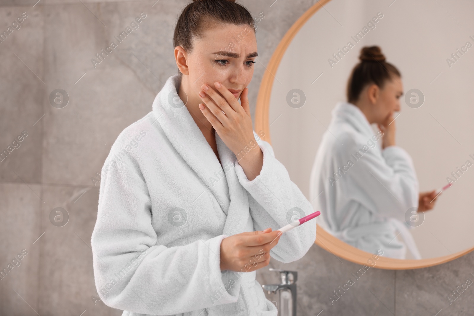 Photo of Sad woman holding pregnancy test in bathroom