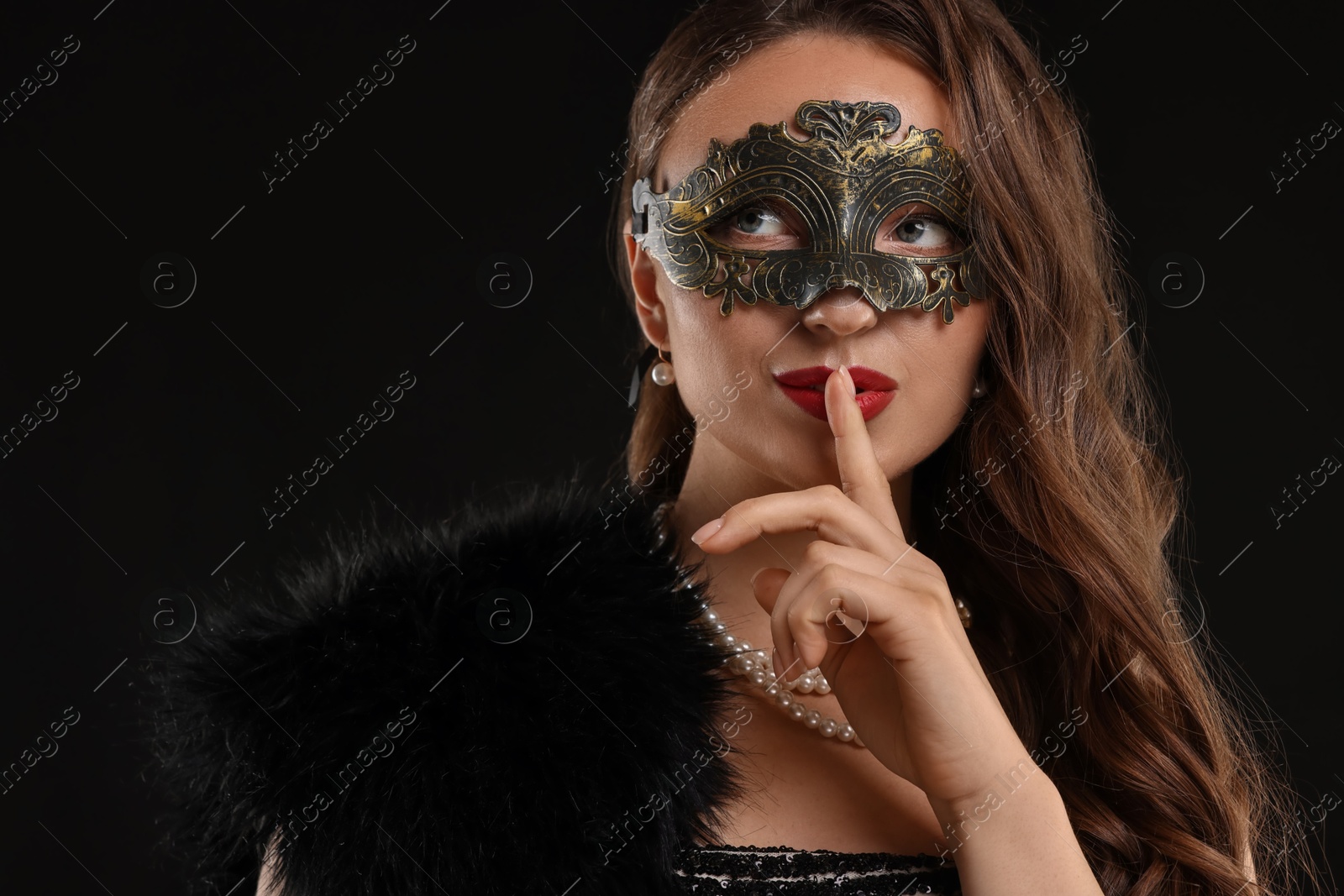 Photo of Beautiful woman wearing carnival mask showing hush gesture on black background