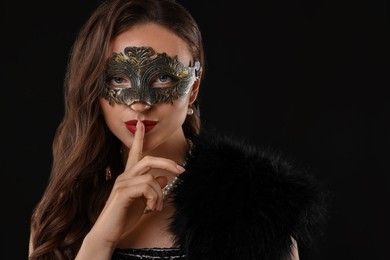 Beautiful woman wearing carnival mask showing hush gesture on black background