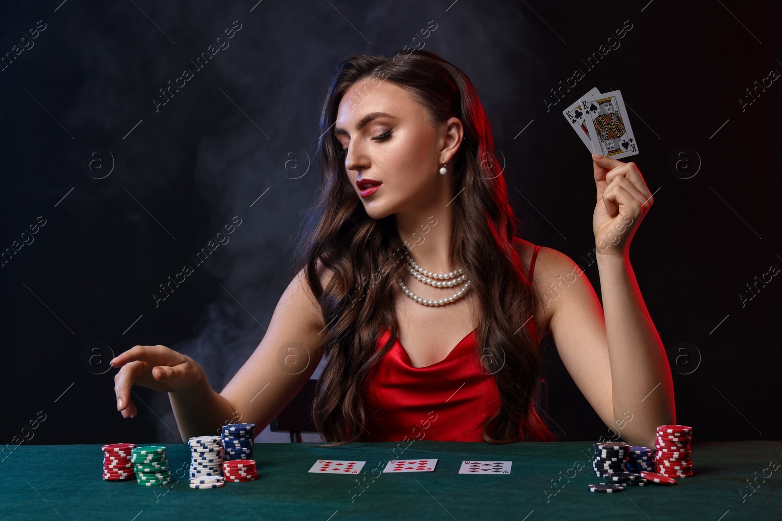 Photo of Charming woman playing poker at table on black background with smoke