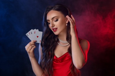 Photo of Poker game. Charming woman with playing cards on black background in color lights and smoke