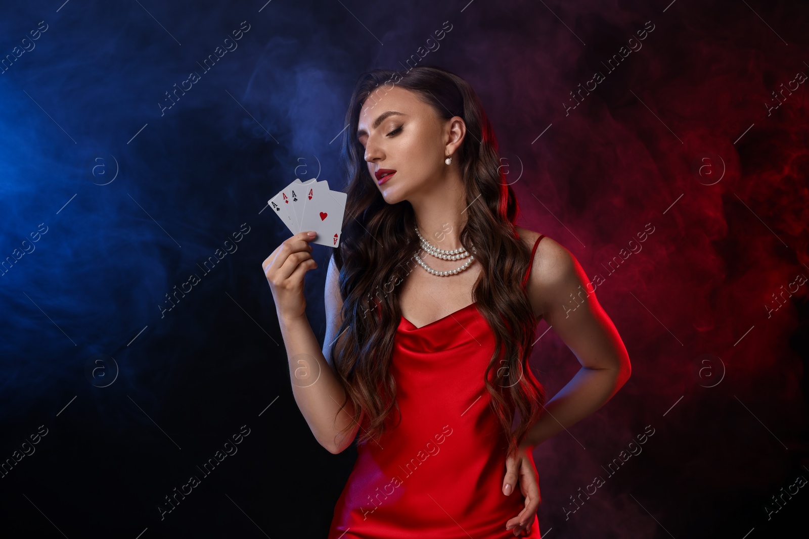 Photo of Poker game. Charming woman with playing cards on black background in color lights and smoke