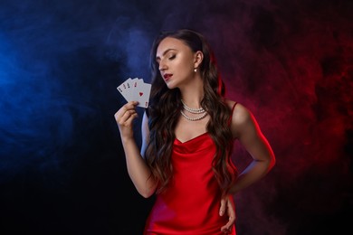 Poker game. Charming woman with playing cards on black background in color lights and smoke