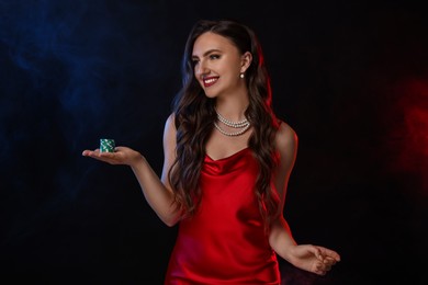 Photo of Smiling woman with poker chips on black background in color lights and smoke