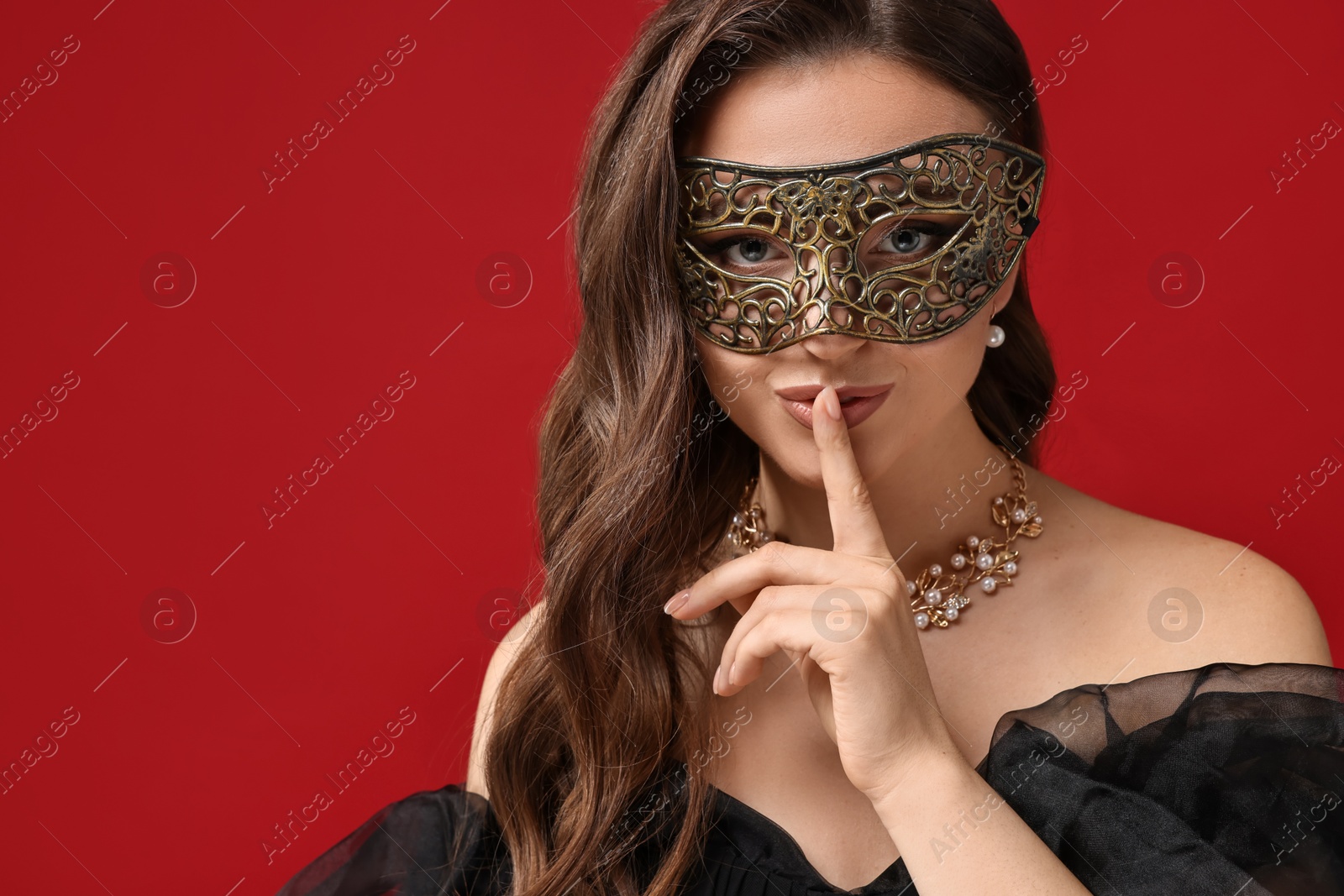 Photo of Beautiful woman with carnival mask showing hush gesture on red background. Space for text