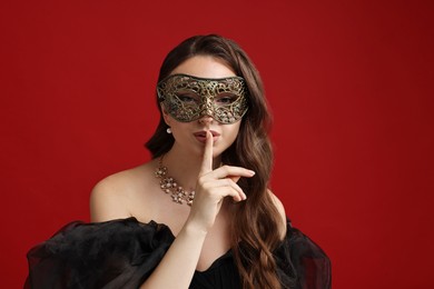 Photo of Beautiful woman with carnival mask showing hush gesture on red background. Space for text