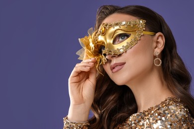 Beautiful woman wearing carnival mask on purple background, closeup. Space for text