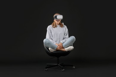 Photo of Happy woman with virtual reality headset sitting on chair against black background