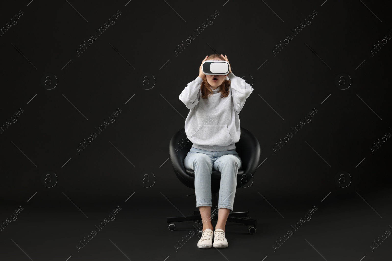 Photo of Emotional woman with virtual reality headset sitting on chair against black background