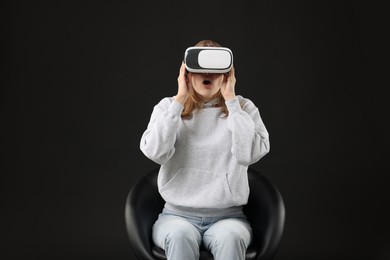 Photo of Emotional woman with virtual reality headset sitting on chair against black background