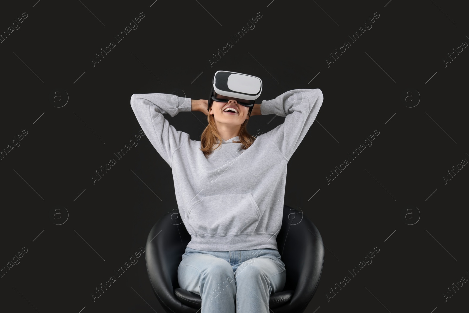 Photo of Happy woman with virtual reality headset sitting on chair against black background