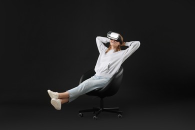 Happy woman with virtual reality headset sitting on chair against black background