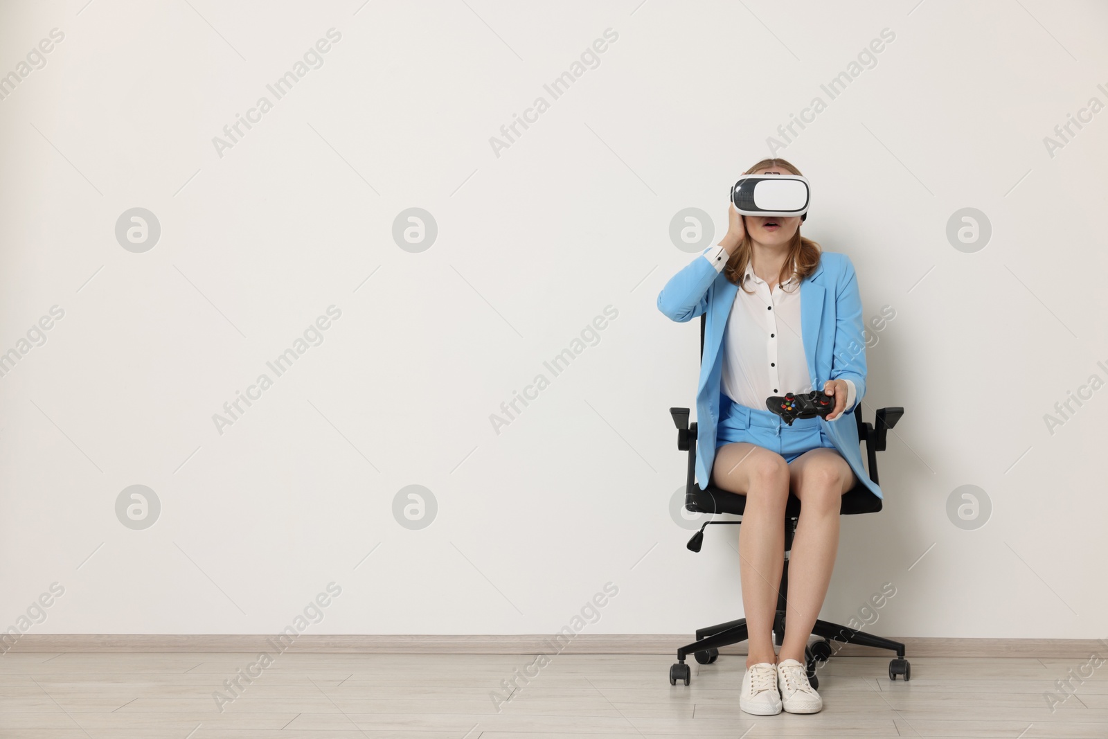 Photo of Emotional woman with virtual reality headset sitting on chair indoors, space for text