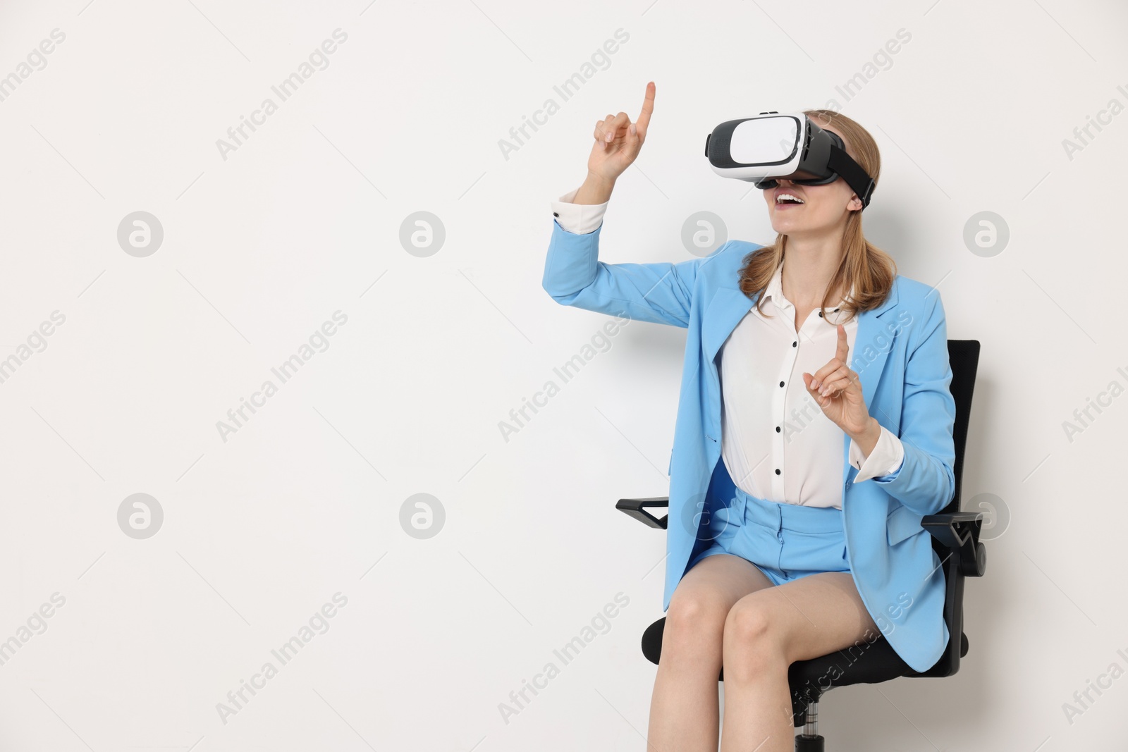 Photo of Happy woman with virtual reality headset sitting on chair against white background, space for text