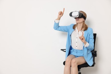 Happy woman with virtual reality headset sitting on chair against white background, space for text