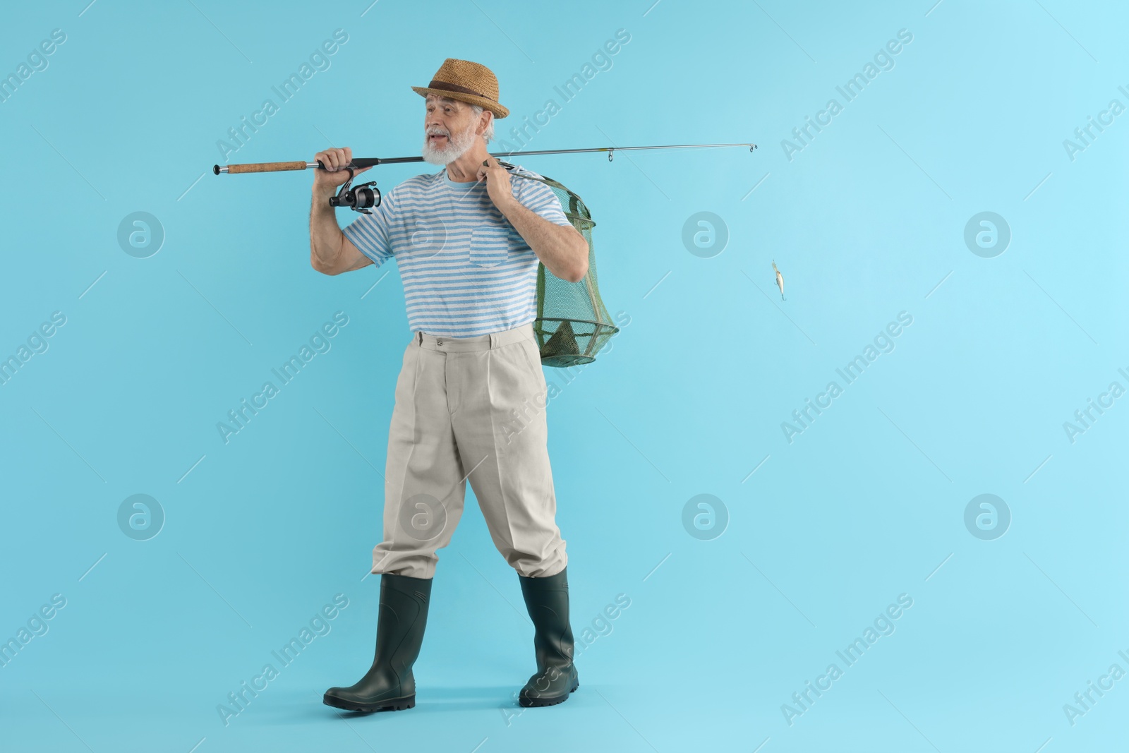 Photo of Fisherman holding rod and fishing net with catch on light blue background