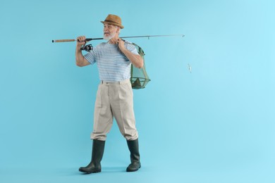 Fisherman holding rod and fishing net with catch on light blue background