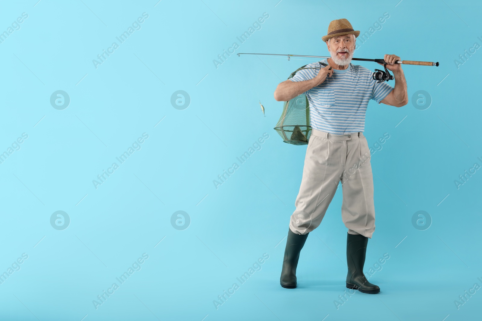 Photo of Fisherman holding rod and fishing net with catch on light blue background