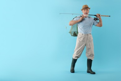 Fisherman holding rod and fishing net with catch on light blue background