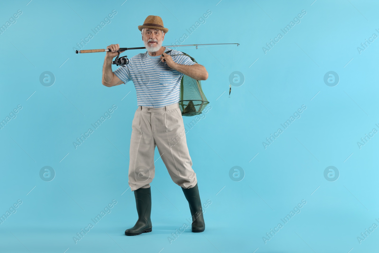 Photo of Fisherman holding rod and fishing net with catch on light blue background