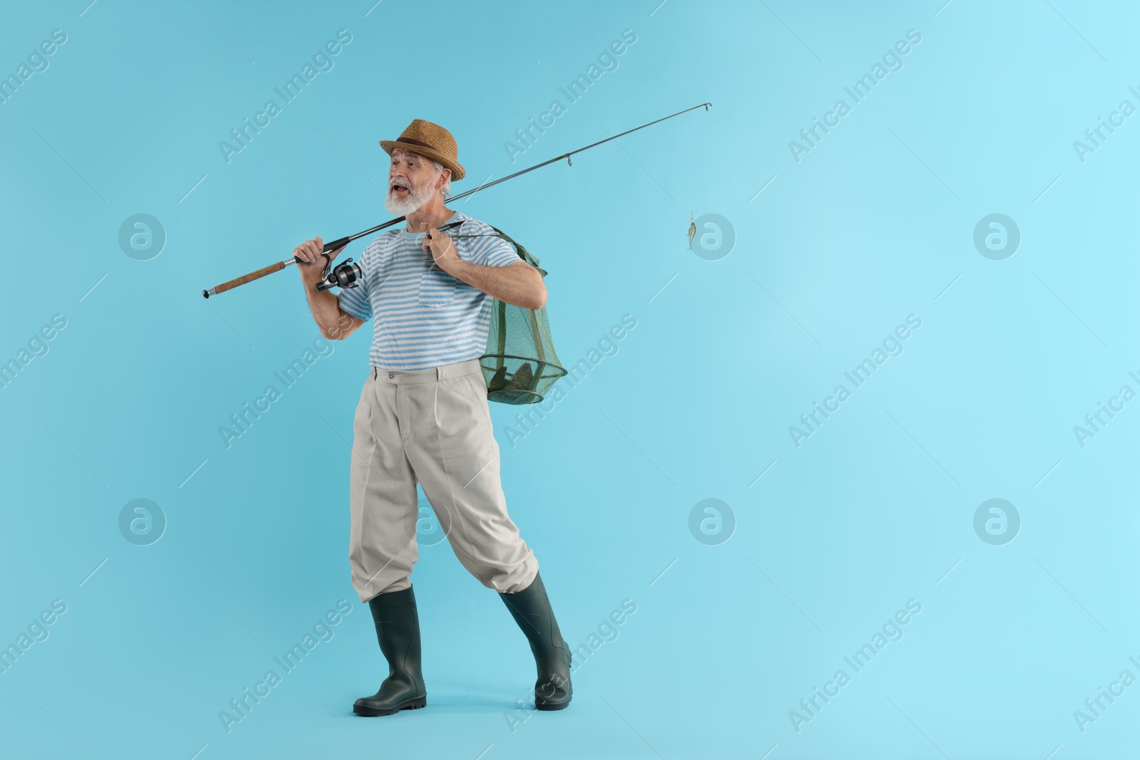 Photo of Fisherman holding rod and fishing net with catch on light blue background