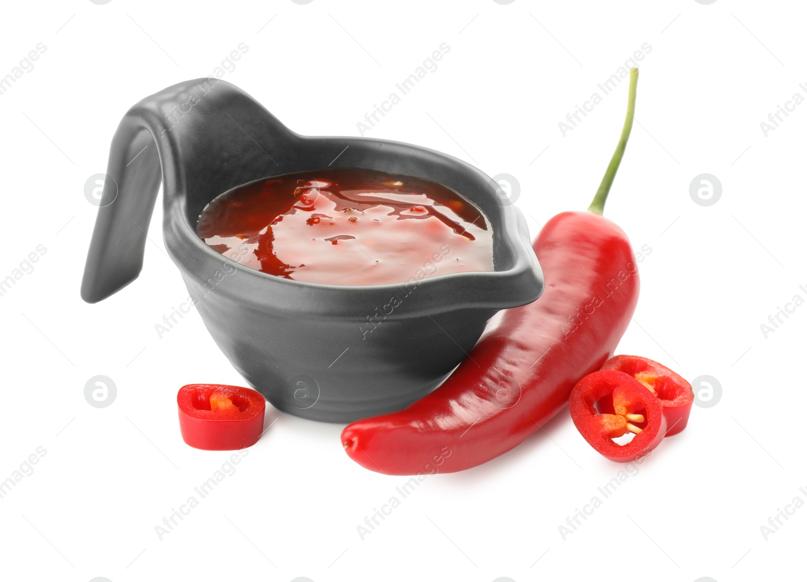 Photo of Hot chili sauce in gravy boat and pepper isolated on white