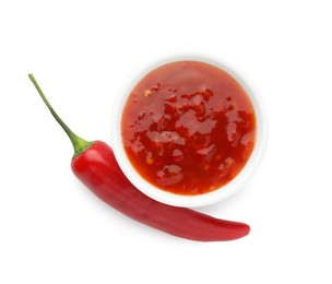 Photo of Hot chili sauce in bowl and pepper isolated on white, top view