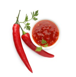 Photo of Hot chili sauce in bowl, parsley and peppers isolated on white, top view