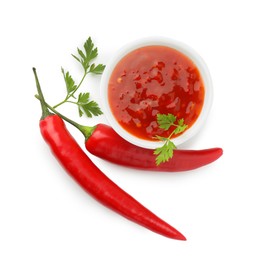 Photo of Hot chili sauce in bowl, parsley and peppers isolated on white, top view