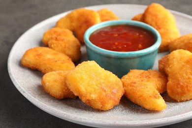 Photo of Plate with hot chili sauce and nuggets on grey table, closeup