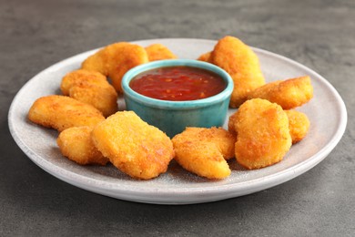 Photo of Plate with hot chili sauce and nuggets on grey textured table, closeup