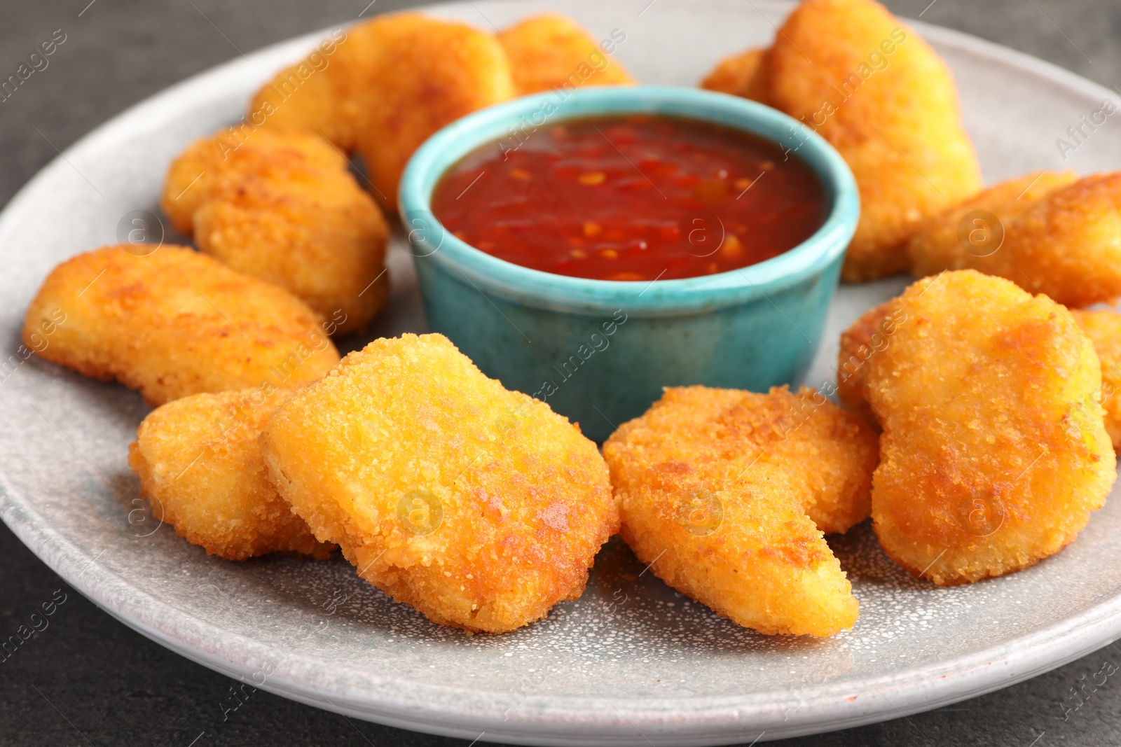 Photo of Plate with hot chili sauce and nuggets on grey table, closeup